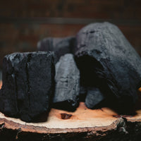 Close-up of black charcoal pieces on a wooden surface with a dark background