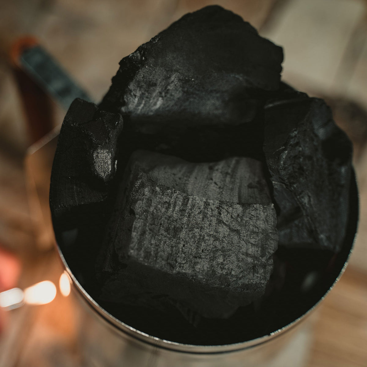 Close-up of black charcoal briquettes in a container with a blurred background