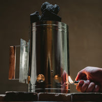 Metal container with charcoal being lit by a hand holding a lighter.