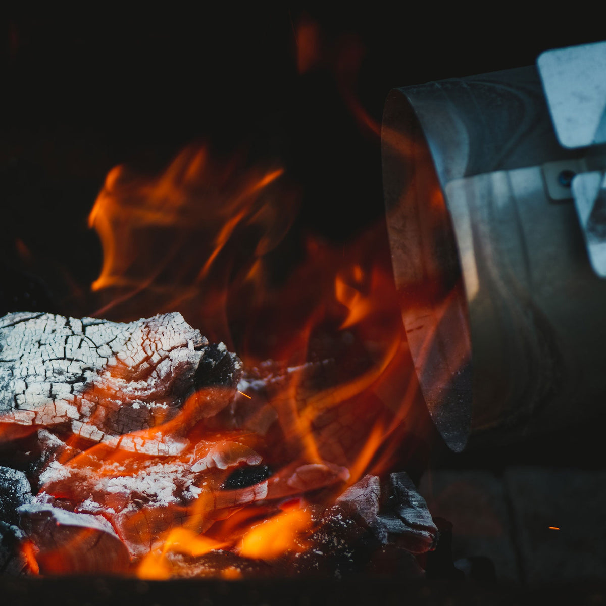 Close-up of a fire with glowing embers and flames, surrounded by dark background.